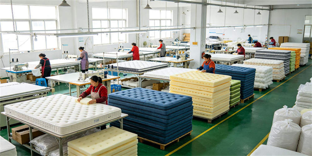 Wide workshop view showing mattress production stations, finished products and organized material handling.