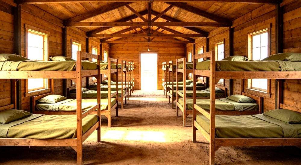 Eye-level interior of agricultural farm worker camp with olive green bedding on simple beds for seasonal harvest labour accommodation in rural areas