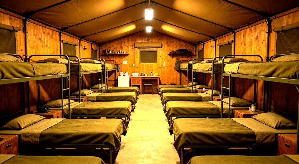 Eye-level interior of remote camp bunkhouse with olive green bedding on wooden frame beds for workers in isolated infrastructure project locations