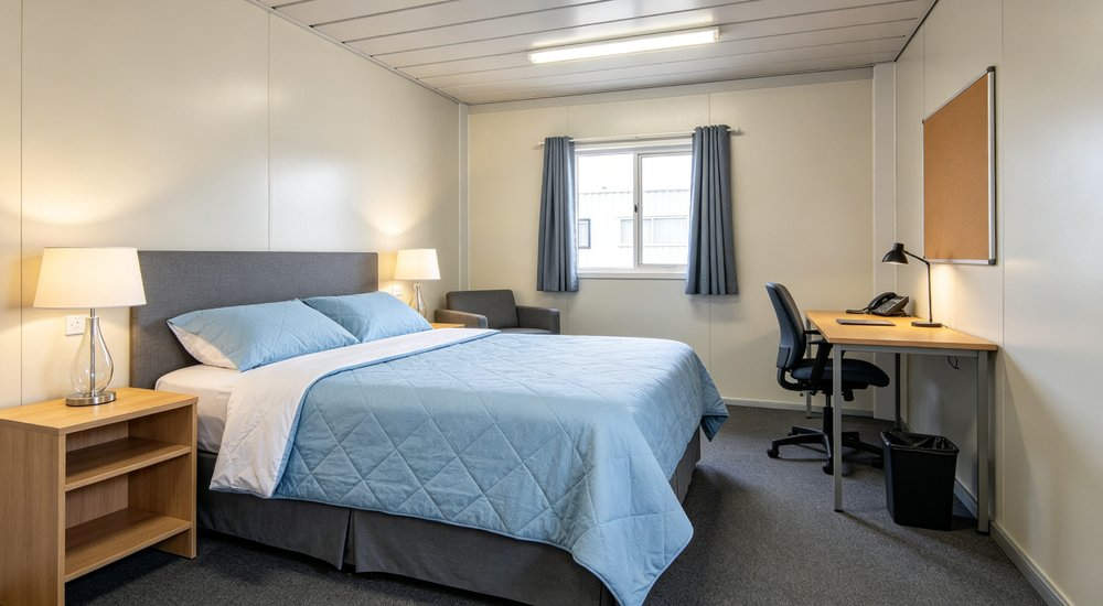 Eye-level interior of camp management quarter with light blue premium bedding on single bed for supervisors and senior staff accommodation