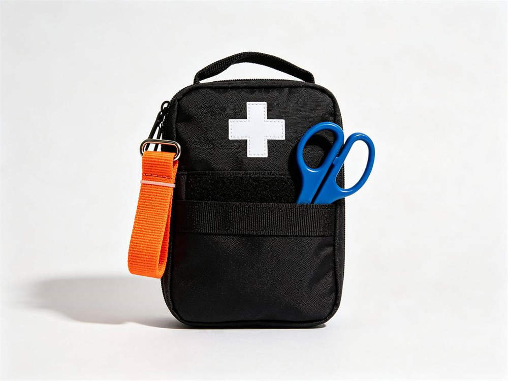 Product shot of basic configuration black medical pouch with white cross orange tourniquet attached and blue trauma shears in side pocket on white background studio display