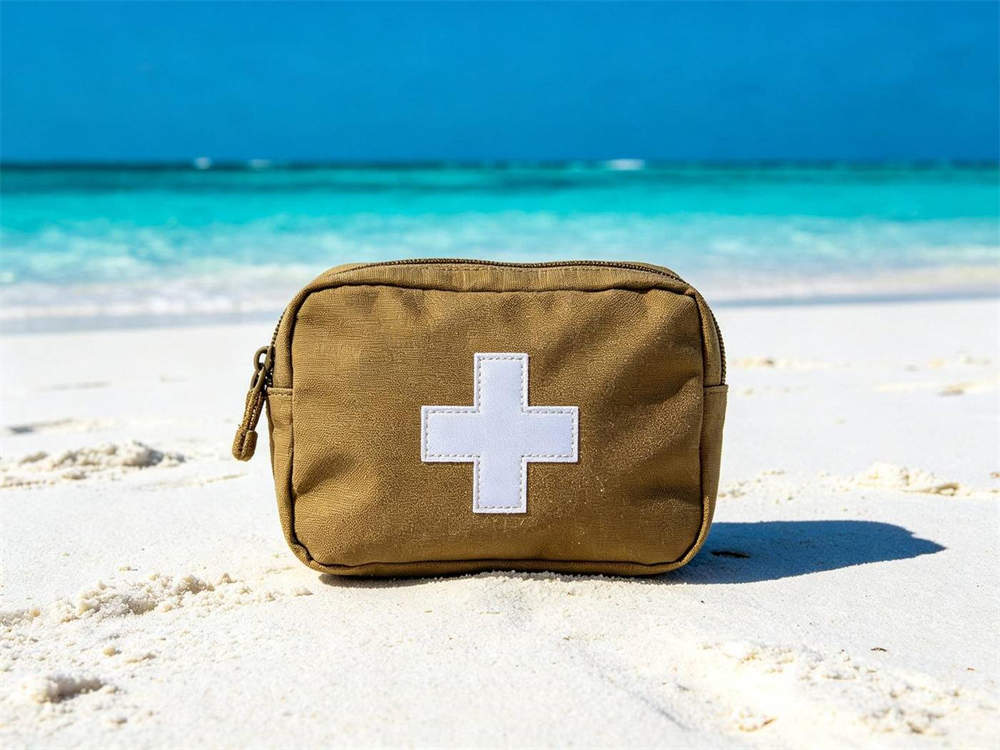 Outdoor beach scene of coyote brown medical pouch with white cross emblem on bright white sandy beach with turquoise ocean background strong color contrast