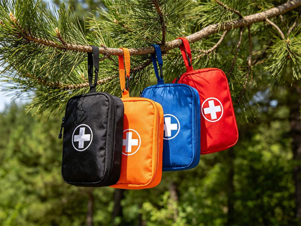 Outdoor forest scene of multiple colored first aid pouches black orange blue and red each with white cross hanging from pine tree branch bright daylight