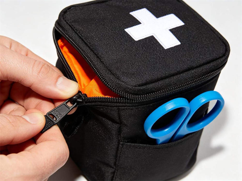 Close up of zipper durability test on black medical pouch with white cross YKK zipper being pulled orange interior visible blue trauma shears in pocket white background