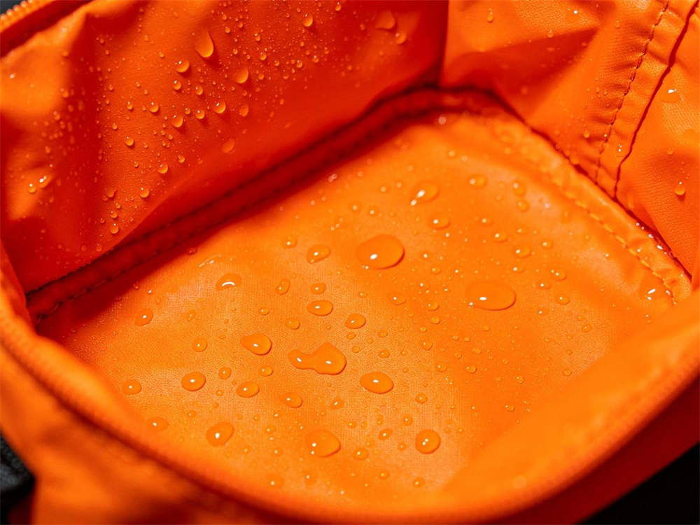 Close up of waterproof interior lining detail on black medical pouch with orange lining and water droplets white background product detail shot
