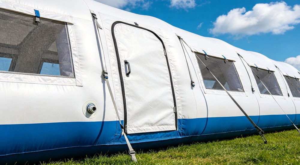 white and blue inflatable tent with zipper door and mesh windows anchored on green grass under blue sky