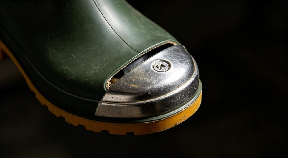 Close-up of 200-joule impact-resistant steel toe cap inside a black safety rain boot, detail view showing ergonomic reinforced protective toe component, industrial safety footwear parts wholesale