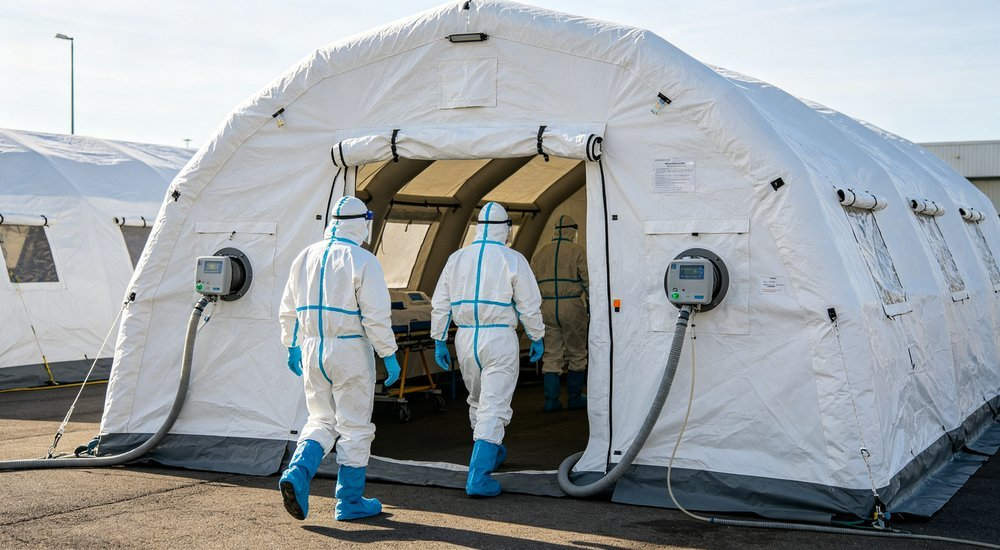 Medium shot of medical staff in full PPE entering contaminated zone of white and blue inflatable isolation tent, negative pressure system visible, professional healthcare photography