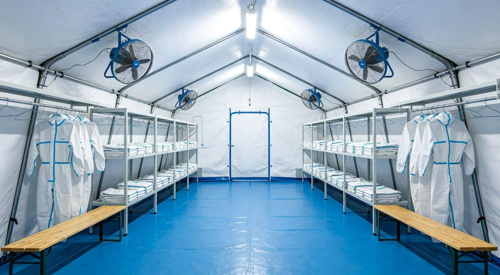 Wide angle shot of decontamination tent certification testing with quality inspector measuring fabric strength and waterproof performance at professional testing facility