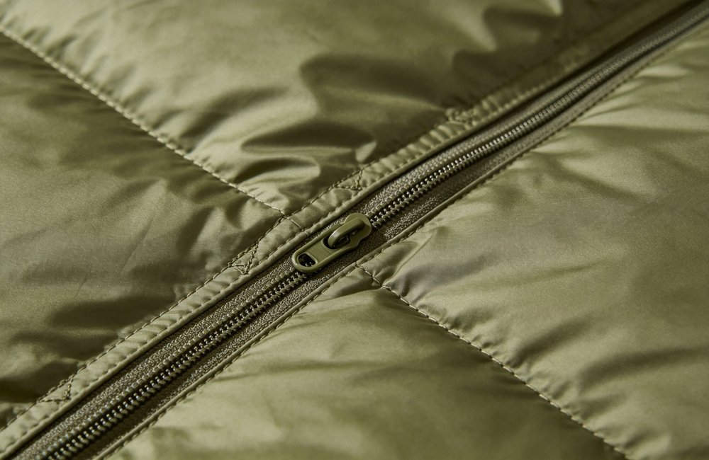 Close-up macro detail of olive green sleeping bag heavy-duty zipper and reinforced stitching, showing durable fabric texture and quality construction, professional product detail photography, no people