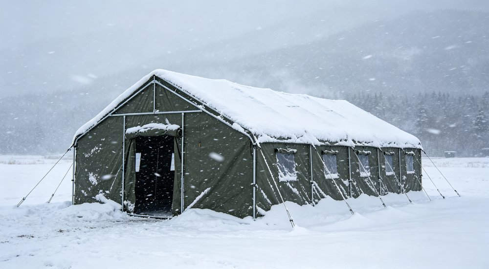 Steel frame relief tent in snowstorm with thick snow covering roof, cold weather performance test in winter landscape, realistic photography
