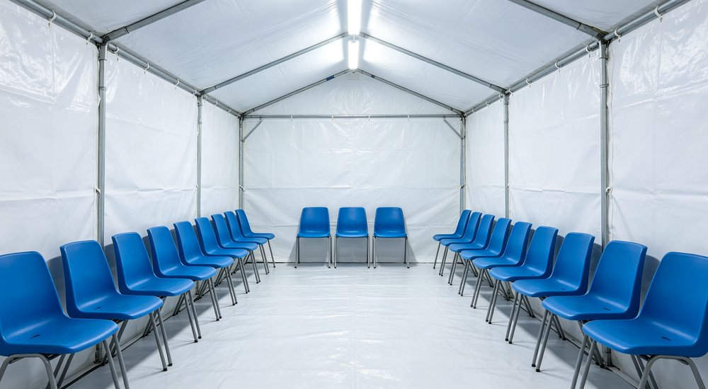 Waiting area inside inflatable medical tent with chairs and patients, bright lighting red and white inflatable emergency shelter for disaster relief operations