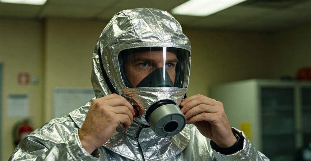 Caucasian adult man demonstrating proper two-hand method of putting on silver aluminum foil smoke escape hood with clear visor during indoor fire safety training
