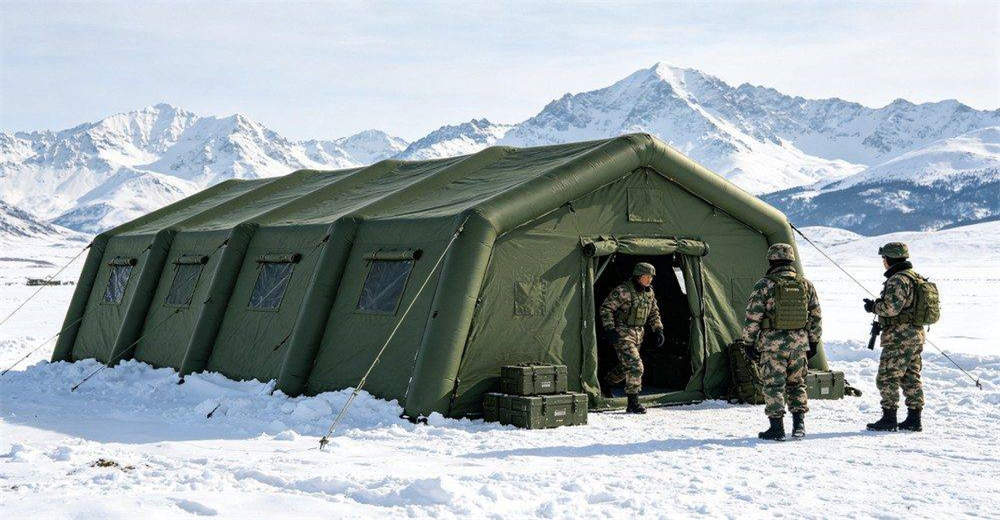 Military inflatable tent in snowy cold environment with snow-covered mountain background, showing tent maintaining structural integrity and providing warm shelter in freezing arctic conditions, demonstrating reliable cold-weather field performance for operations