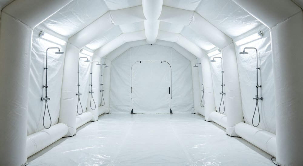 Decontamination air beam tent, external air beams visible, workers, green grass red and white inflatable emergency shelter for disaster relief operations