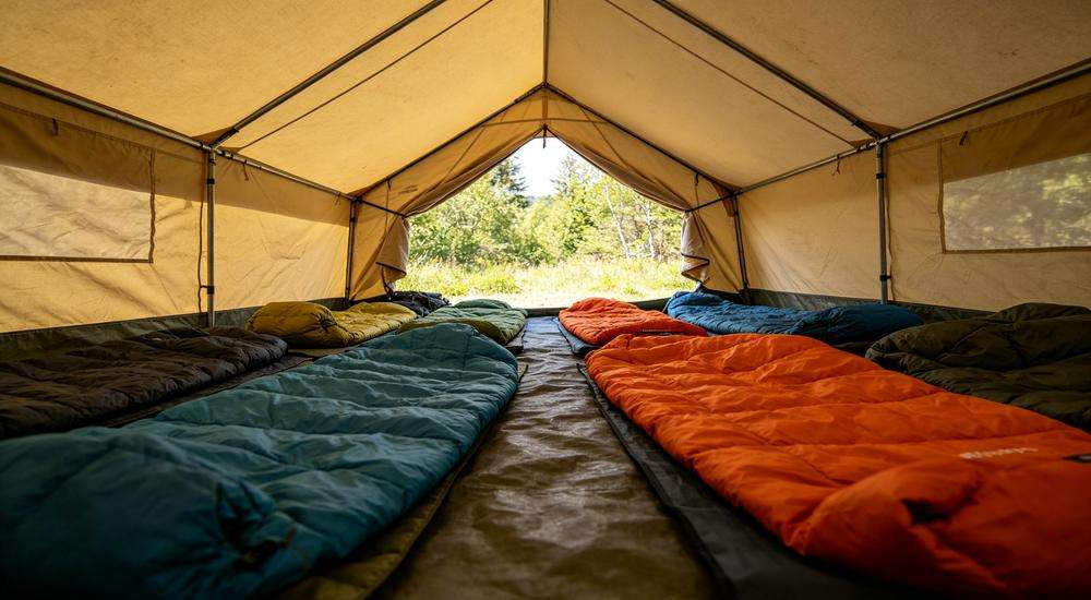 Wide angle view of tent interior with sleeping bags arranged, outdoor semi-exposed emergency shelter condition, natural daylight inside tent
