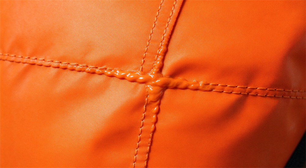 Product macro detail of welded seam construction on orange ice rescue suit showing polyurethane coating fusion at seam junction for waterproof integrity