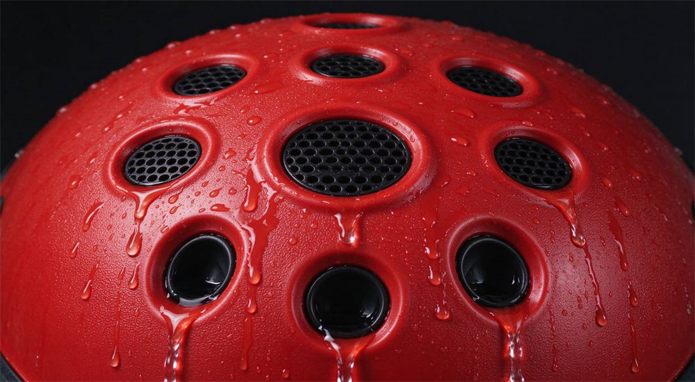 Macro detail of water rescue helmet top showing multiple circular drainage and ventilation vents arranged in pattern on red ABS shell, 8-10 recessed angled ports with water droplets draining from vents