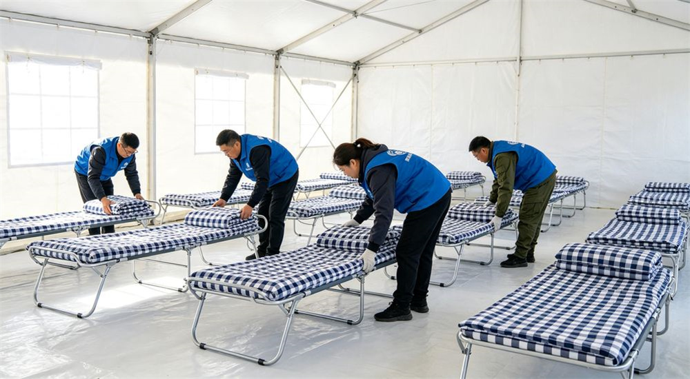 Overhead view of relief workers in vests distributing navy check emergency relief bedding packs in an aid warehouse, rapid deployment humanitarian bedding logistics and distribution operations, during an organized aid release to displaced beneficiary families.