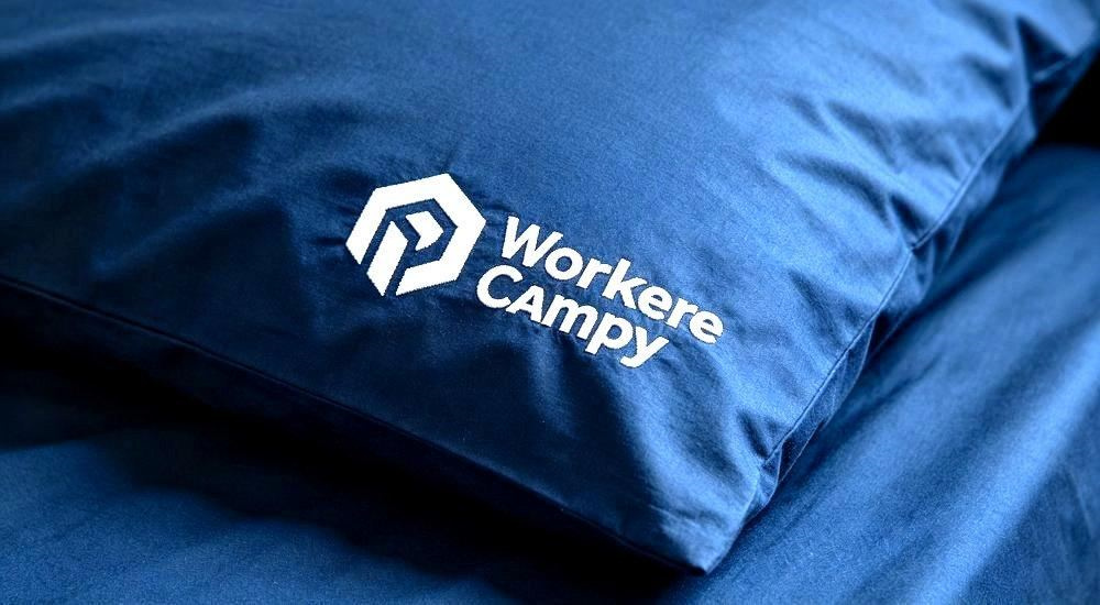 Custom logo embroidery closeup on navy workforce camp bedding pillowcase, branded identity detail for construction and mining camp linen programs, wholesale durable dormitory bedding customization option stitched neatly in white thread