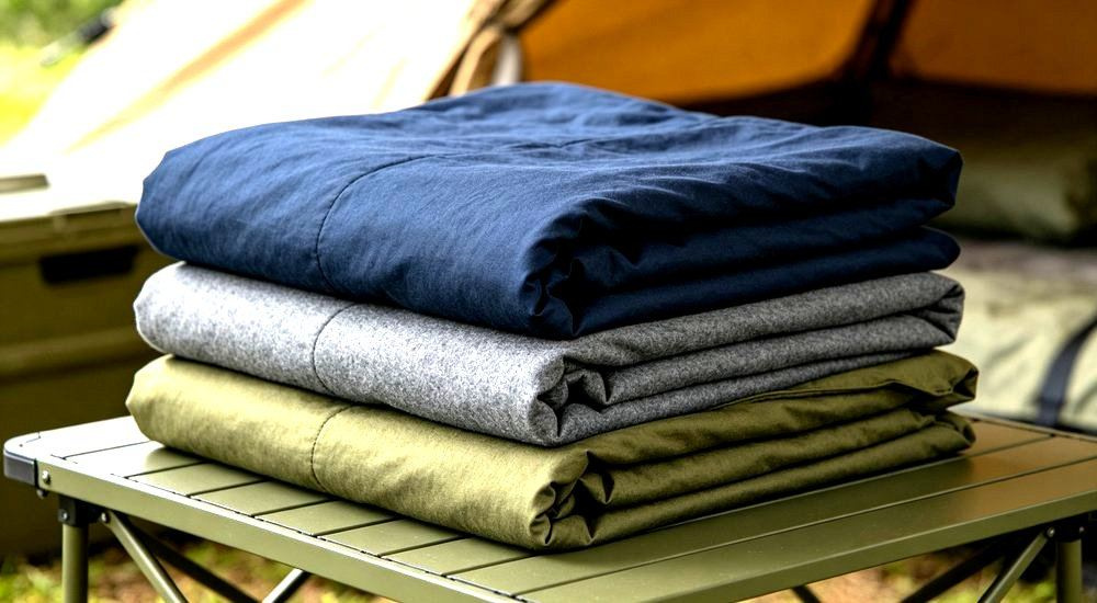 45-degree angle of dark color options of workforce camp bedding folded on a table, navy olive and gray stain hiding shades for practical camp linen for construction camp bedding buyers sourcing durable linen.