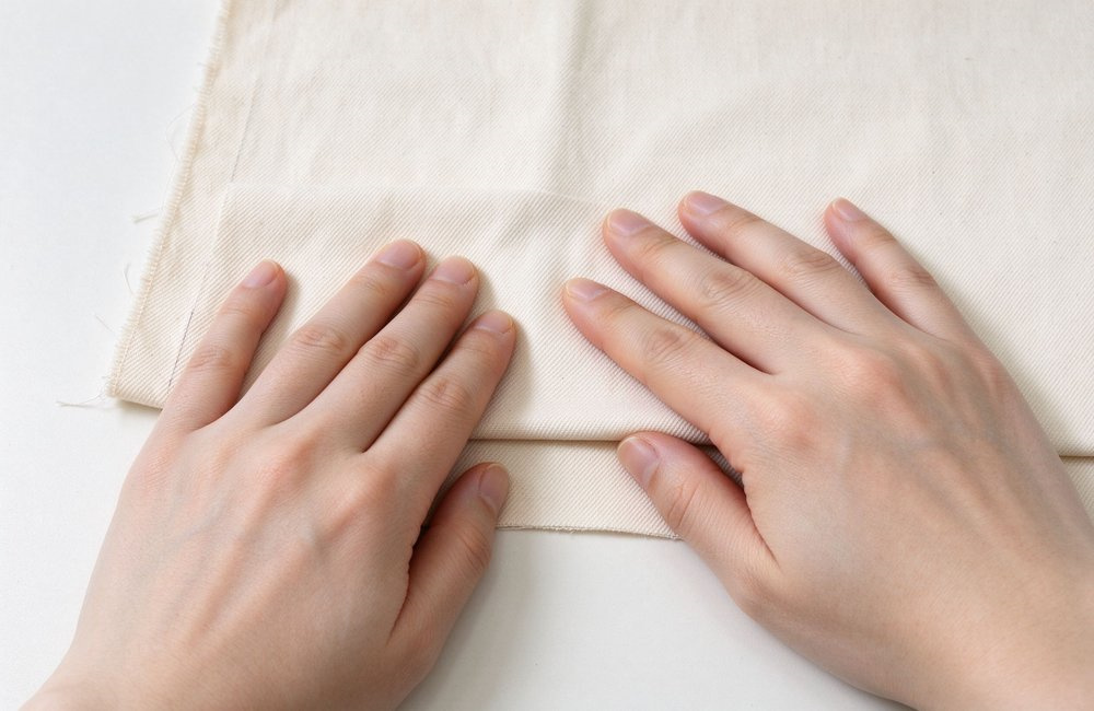 Close-up of hands rubbing two cotton fabric swatches on an inspection desk to test institutional bulk bedding wholesale durability, light versus heavy twill