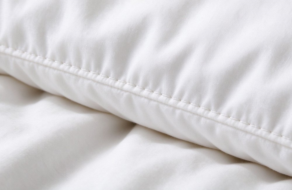 Close-up view of neat even stitching on a white institutional bulk bedding wholesale duvet cover seam, quality inspection detail under soft light