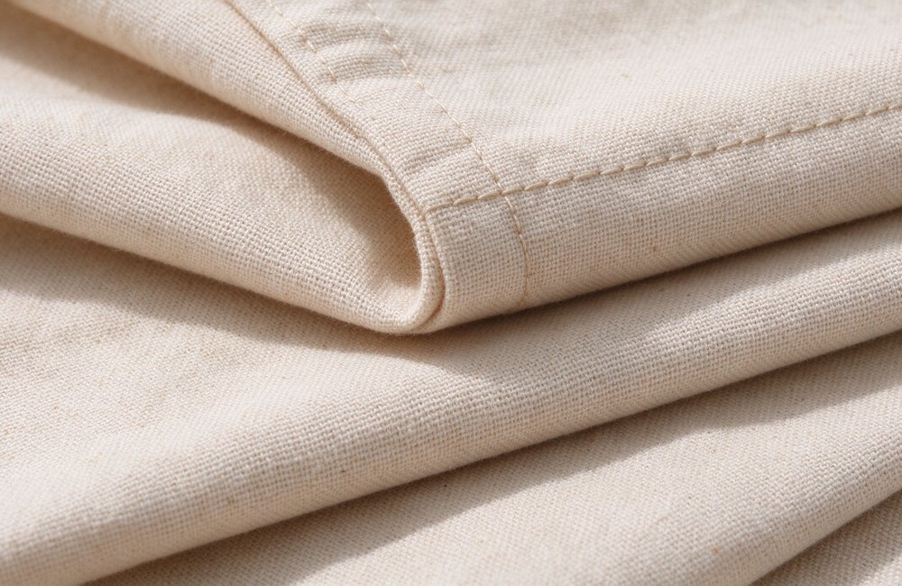 Close-up of folded beige cotton fabric layers showing tight weave and stitched edge on institutional bulk bedding wholesale, colour and GSM detail