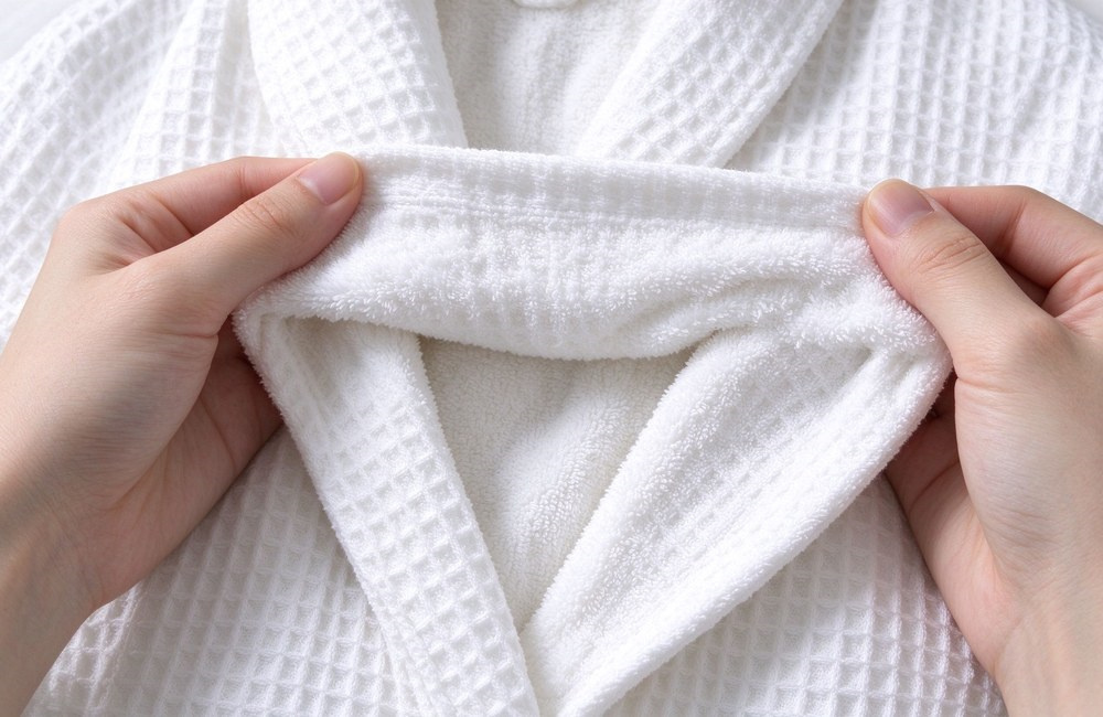 Hands opening double layer bathrobe fabric showing waffle weave outer layer and terry inner layer, comparing breathable and absorbent construction for spa robes
