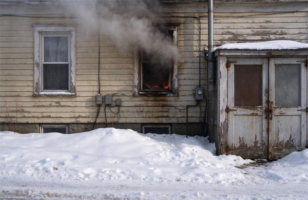Old house with smoke coming from window during winter, dangerous unvented heating scenario, carbon monoxide poisoning risk and emergency heating safety warnings