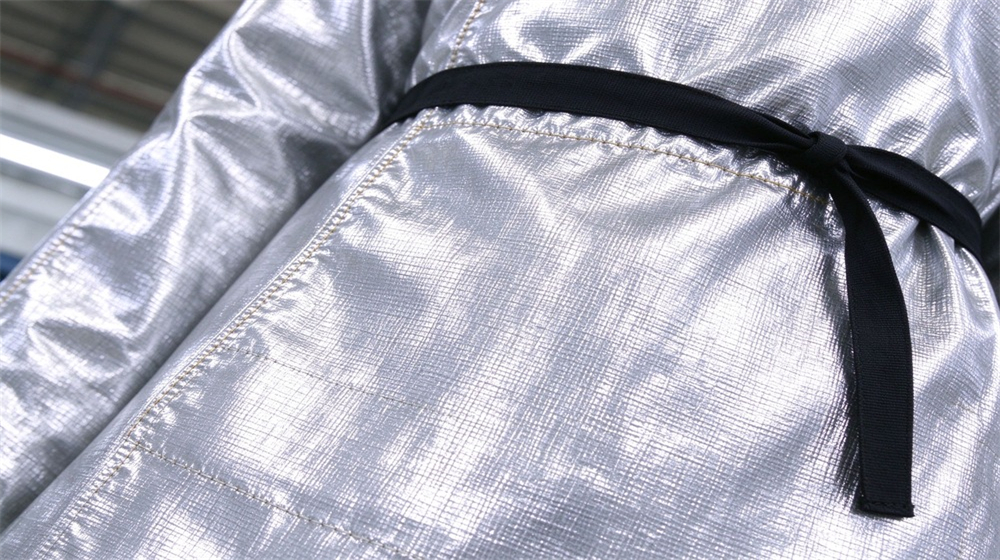 Wide shot of heavy duty protective heat resistant apron arm guards, Heat resistant apron edge stitching and black tie detail on aluminum foil, demonstrating professional info use in industrial safety environment, designed for wholesale bulk supply and industrial safety procurement.