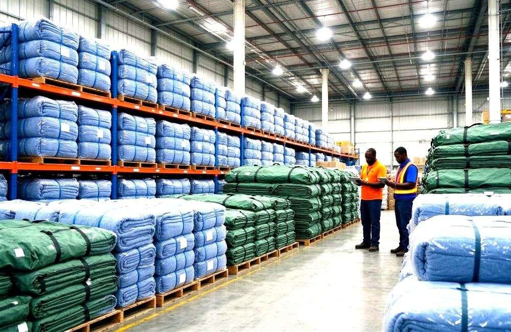 Bright relief warehouse with stacked cartons of responder workwear and blankets ready for field deployment, showing medical relief supplies bulk stock planning
