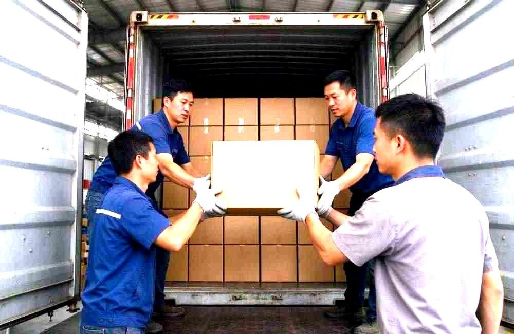 Workers loading responder workwear and blanket cartons into a shipping container for Africa, showing field deployment relief packing and export logistics