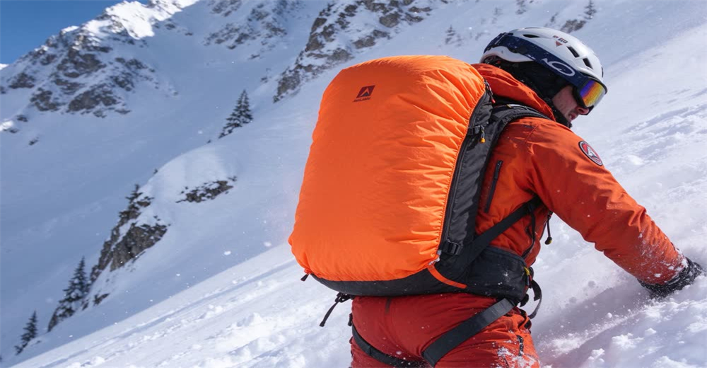 Wide view of rescuer with deployed avalanche airbag on snowy slope showing airbag keeping victim on surface
