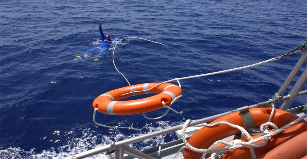Wide view of crew throwing rescue rope to person overboard during maritime drill showing man overboard recovery