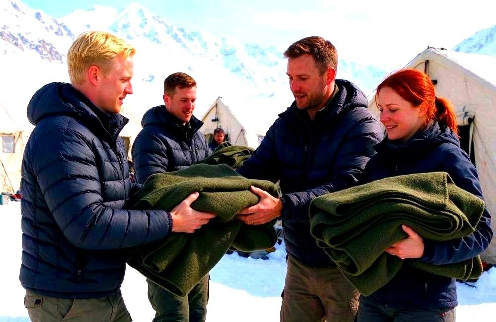 Wide view of a European rescue team using olive-coloured field blankets at an outdoor cold-weather camp, relief blankets for emergency field operations in harsh conditions